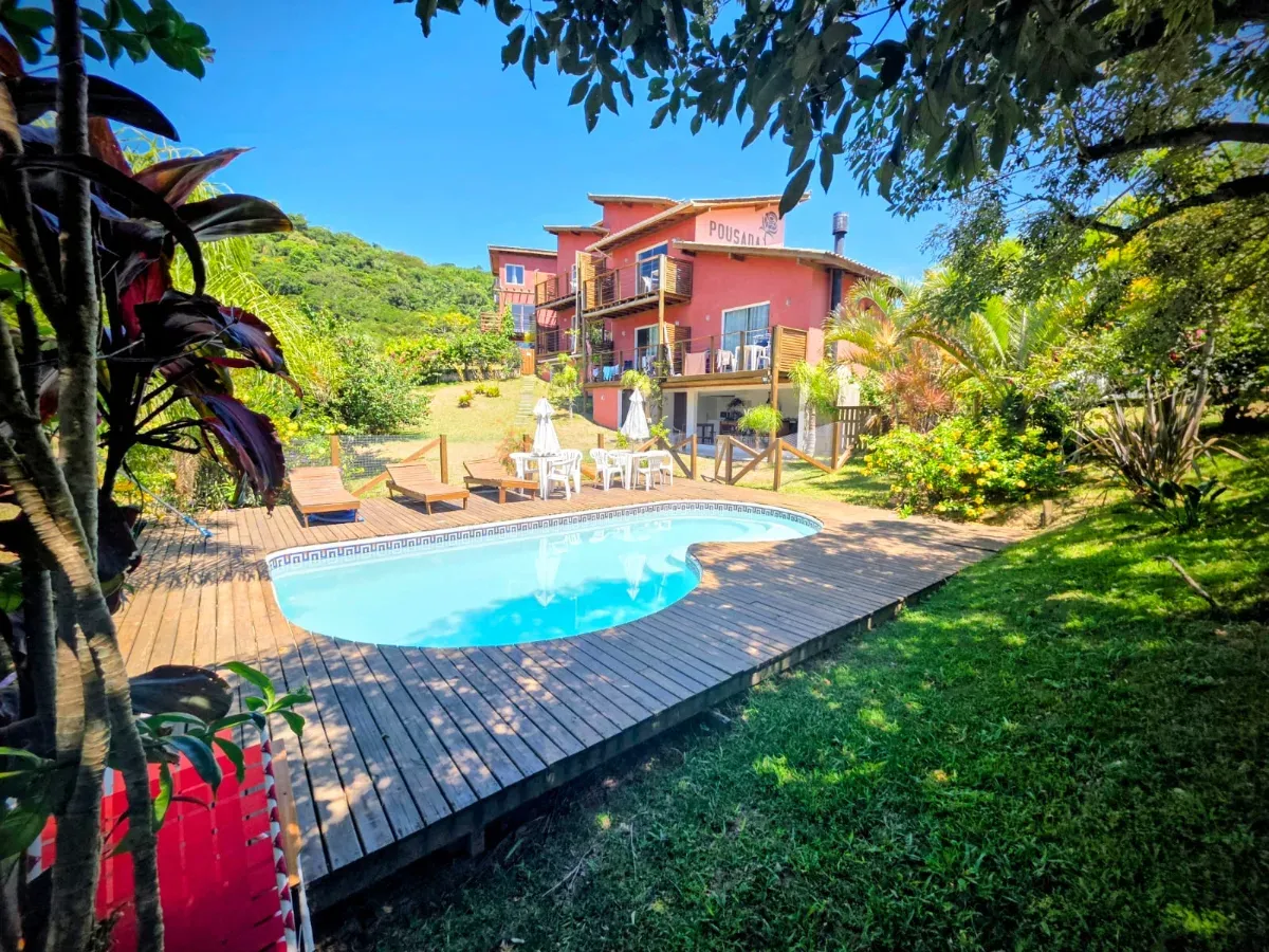 Piscina e deck de madeira da Pousada Rosa Negra em dia de sol, com o prédio rosa ao fundo